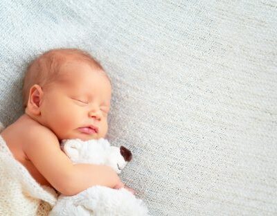 a newborn baby sleeping on a whit blanket, wrapped in a whit blanket, baby is snuggling a white teddy bear