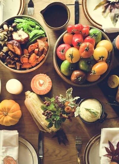 a wood table with all the fixings of an epic thanksgiving dinner including bread, vegetables, a roasted turkey, place settings, a salad, etc.