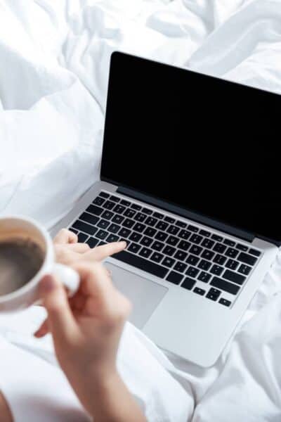 woman in bed drinking coffee working on her budget on the computer