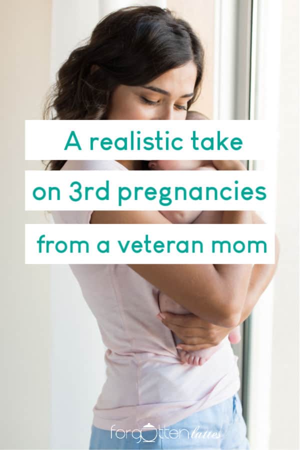 a woman in a pink shirt is standing by a window hugging her newborn baby, the text overlay reads "a realistic take on 3rd pregnancies from a veteran mom"